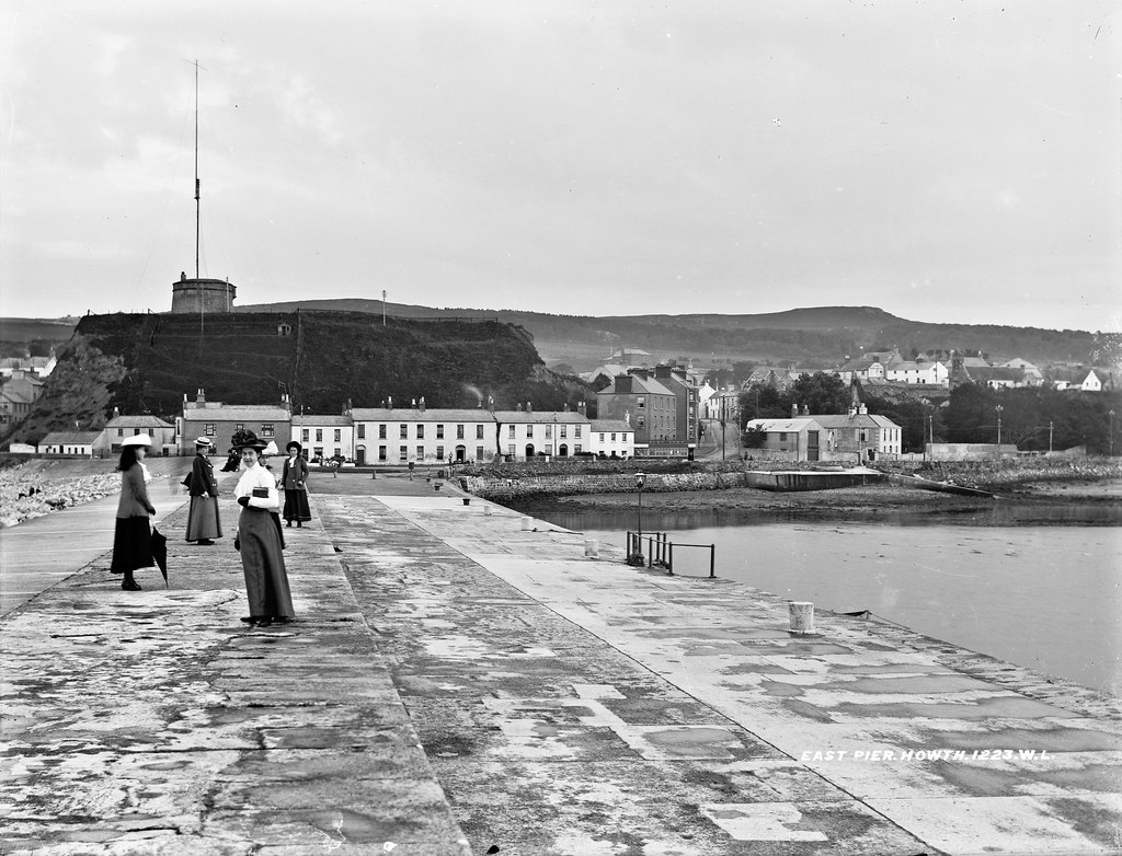 Vintage black-and-white women in long skirts and hats on a stone pier overlooking town and tower. — illustrating “The Demise of the Car Boot Sale” on Florence and Mary