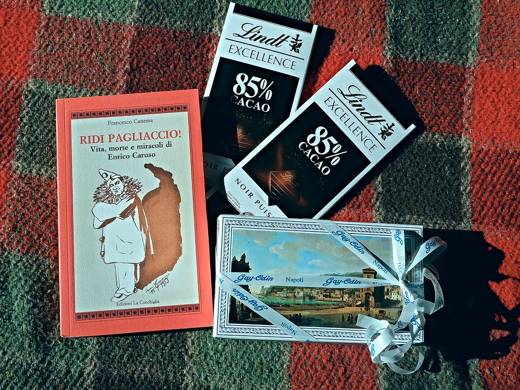 Red-bordered book, two Lindt dark chocolate bars, and ribbon-tied gift box on textured red-green rug. — illustrating “The Khardashian's Stocking Fillers” on Florence and Mary