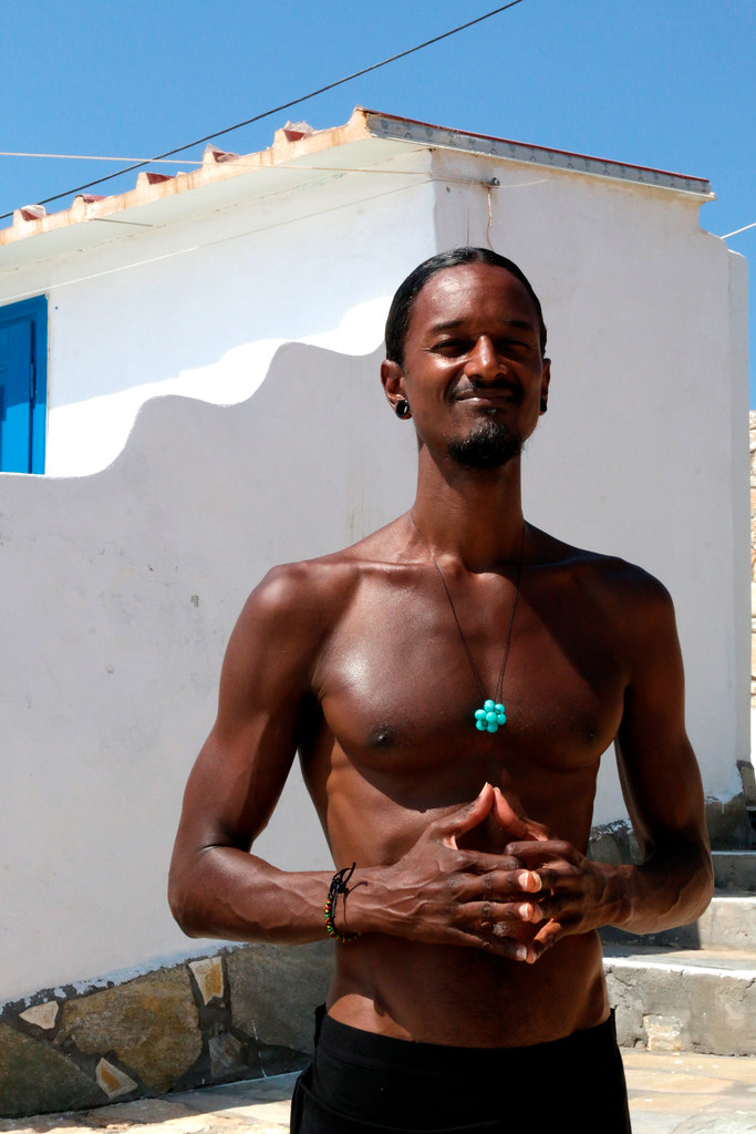 Shirtless athletic dark-skinned man smiles with clasped hands before a white building and blue sky. — illustrating “The Swarovski USB Pen in Fuchsia” on Florence and Mary