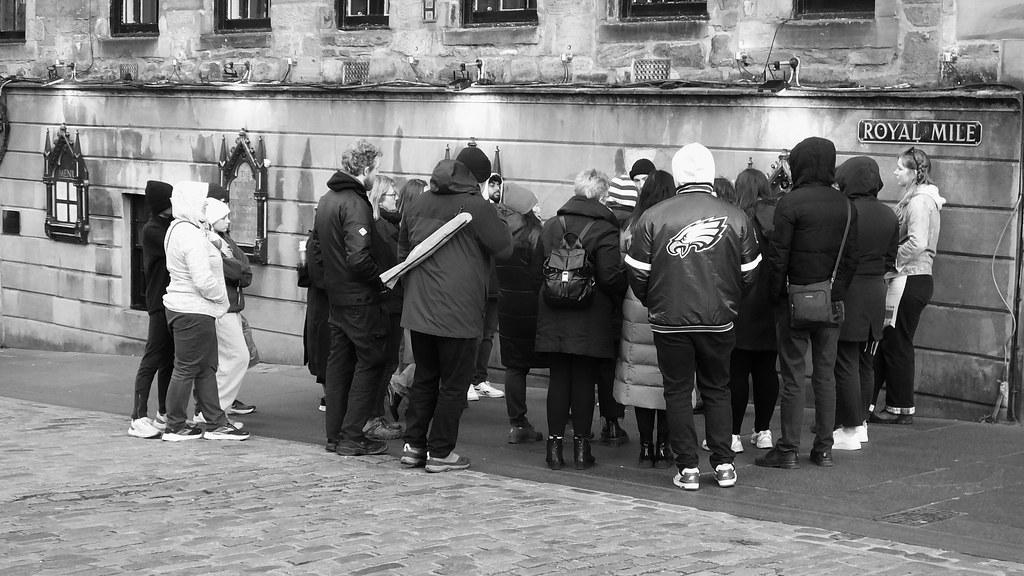 Black-and-white photo of people in warm coats gathered on cobblestones beside a Royal Mile sign. — illustrating “The Witchery, Edinburgh” on Florence and Mary