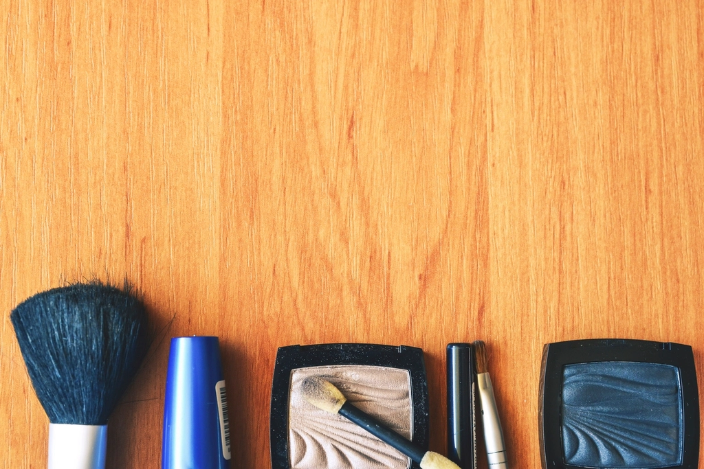 Makeup brushes, a blue tube, and two eyeshadow palettes arranged along a light-brown wooden tabletop. — illustrating “#theSOproject // Week 3 Foundation” on Florence and Mary