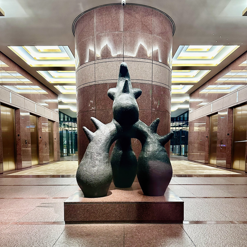 Dark abstract sculpture with pointed protrusions in a pink marble lobby between golden elevator doors. — illustrating “US Drugstore & 200 Follower Giveaway” on Florence and Mary