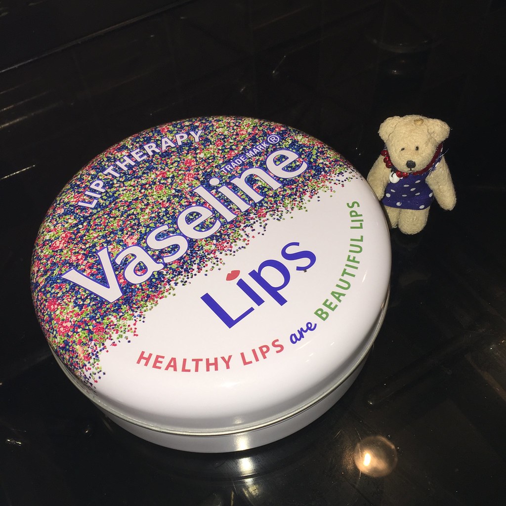 Large white Vaseline Lip Therapy tin with confetti sits beside a tiny teddy bear on black glass. — illustrating “Vaseline Queen Bee” on Florence and Mary