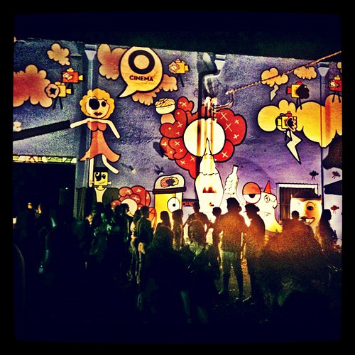 A nighttime crowd gathers before a colorful outdoor mural of cartoon characters and a cinema logo. — illustrating “Week 49 // The Silly Season” on Florence and Mary