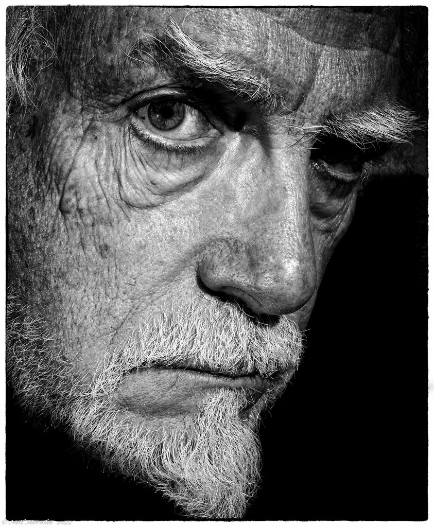 A high-contrast black-and-white close-up of an elderly man with white eyebrows and pointed goatee. — illustrating “Wilkinson Sword Quattro Bikini Razor” on Florence and Mary